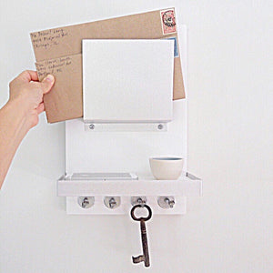 All white mail holder mounted on the wall with an iphone and flower pot on the shelf.