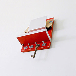 Angled shot from below of the red mail holder showcasing the key hooks and attached wooden shelf with metallic border walls.